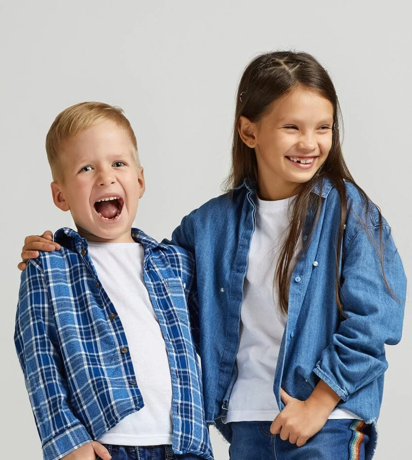 A smiling boy and girl in denim and plaid standing arm in arm